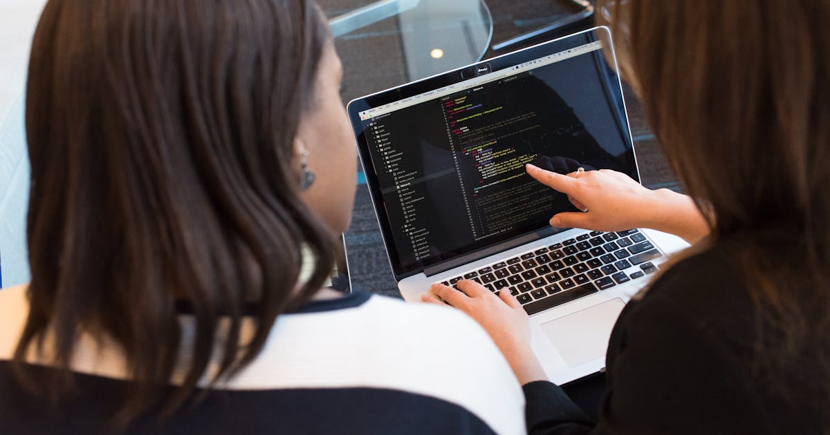 Two developers reviewing code together on a laptop screen during a pair programming session